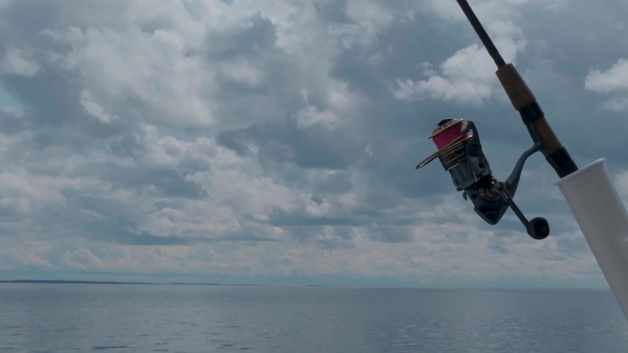 La barca si muove stabilmente sul lago mentre una canna da pesca rimane a fuoco sullo sfondo del paesaggio che scorre