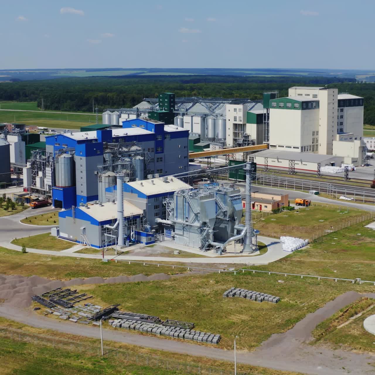 Modern silos on field. Industrial zone for grain storage among green nature. Warehouse for agribusiness in the countryside. Aerial view.