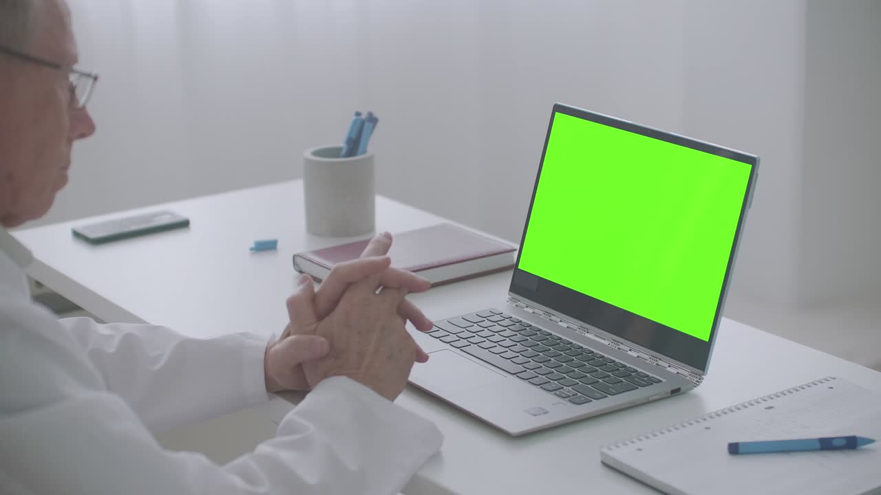 médico masculino está consultando en línea, mirando la pantalla verde de la computadora portátil en la oficina de la clínica, tecnología de clave de croma