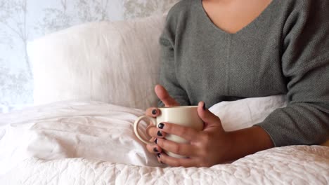 young woman drinking a cup of tea in bed