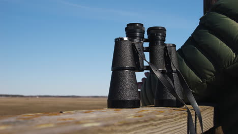 person sets binoculars on watch tower rail and looks out