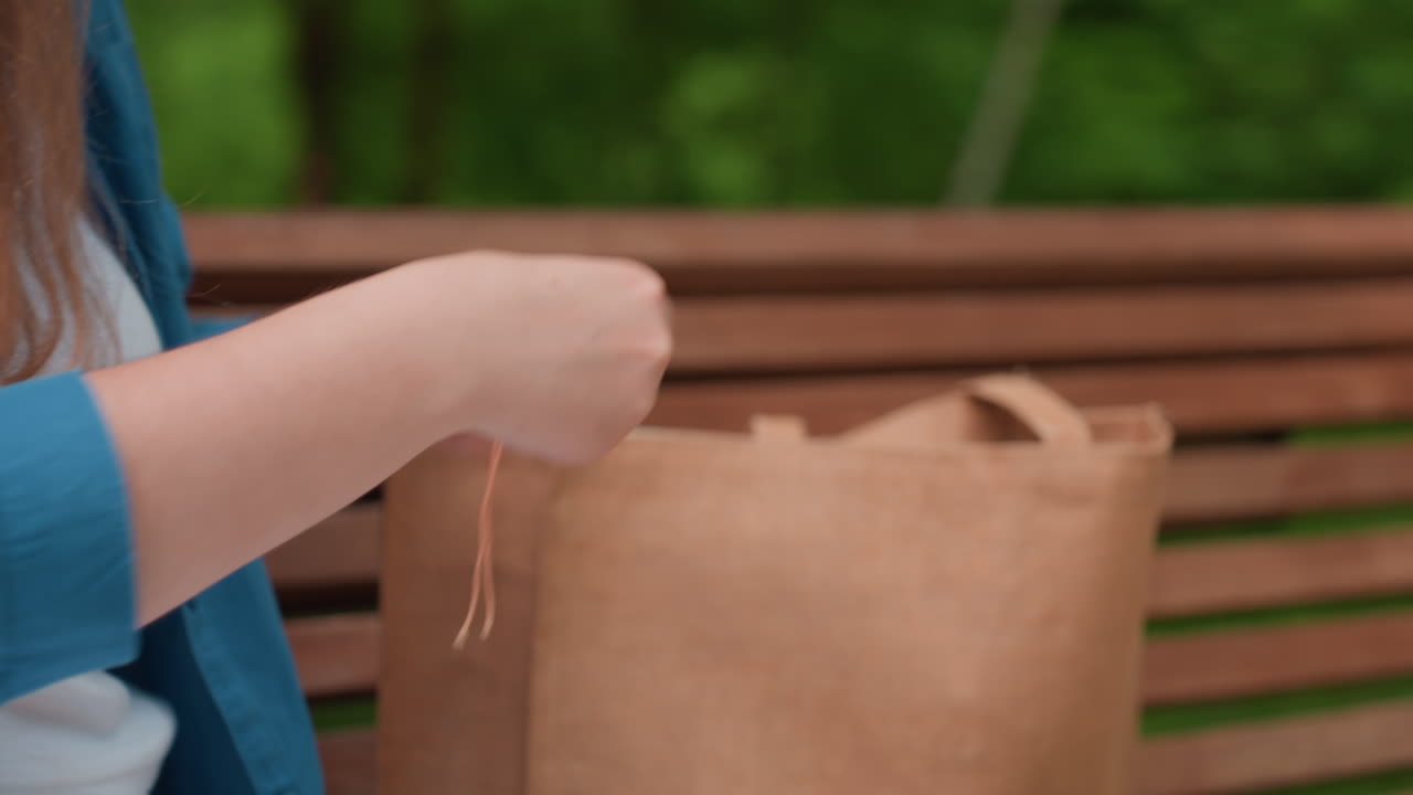 Close up of woman rolling colorful embroidery threads on paper organizer while sitting outdoors, preparing materials for handcraft project with focus on fingers