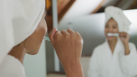 Mixed-race-woman-looking-at-mirror-brushing-teeth