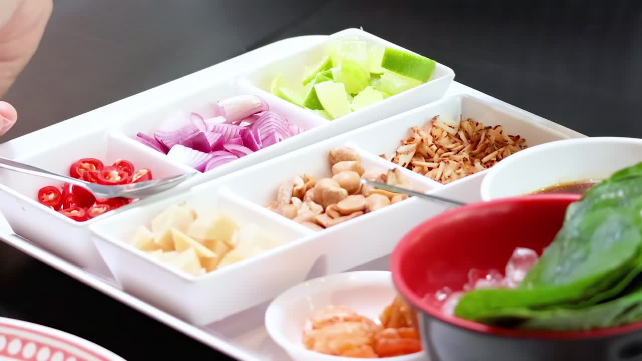 Close-up of hands preparing leaf wraps with assorted fresh ingredients in a tray.