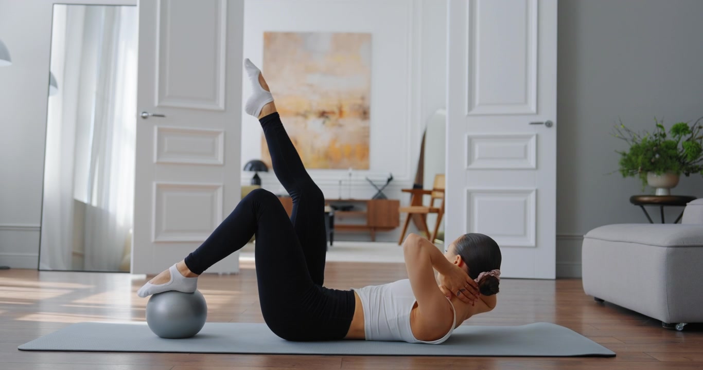 Giovane donna che esegue un esercizio Pilates per il core con una piccola palla a casa