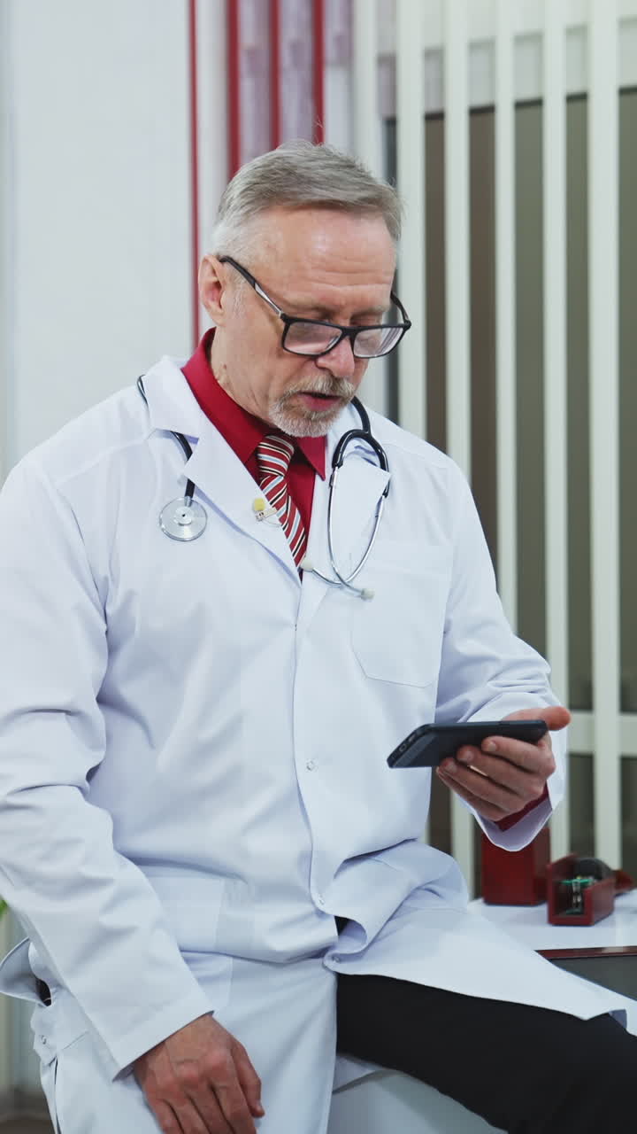 Confident family therapist working online. Doctor in white gown consulting people via internet using mobile phone in the office. Vertical video