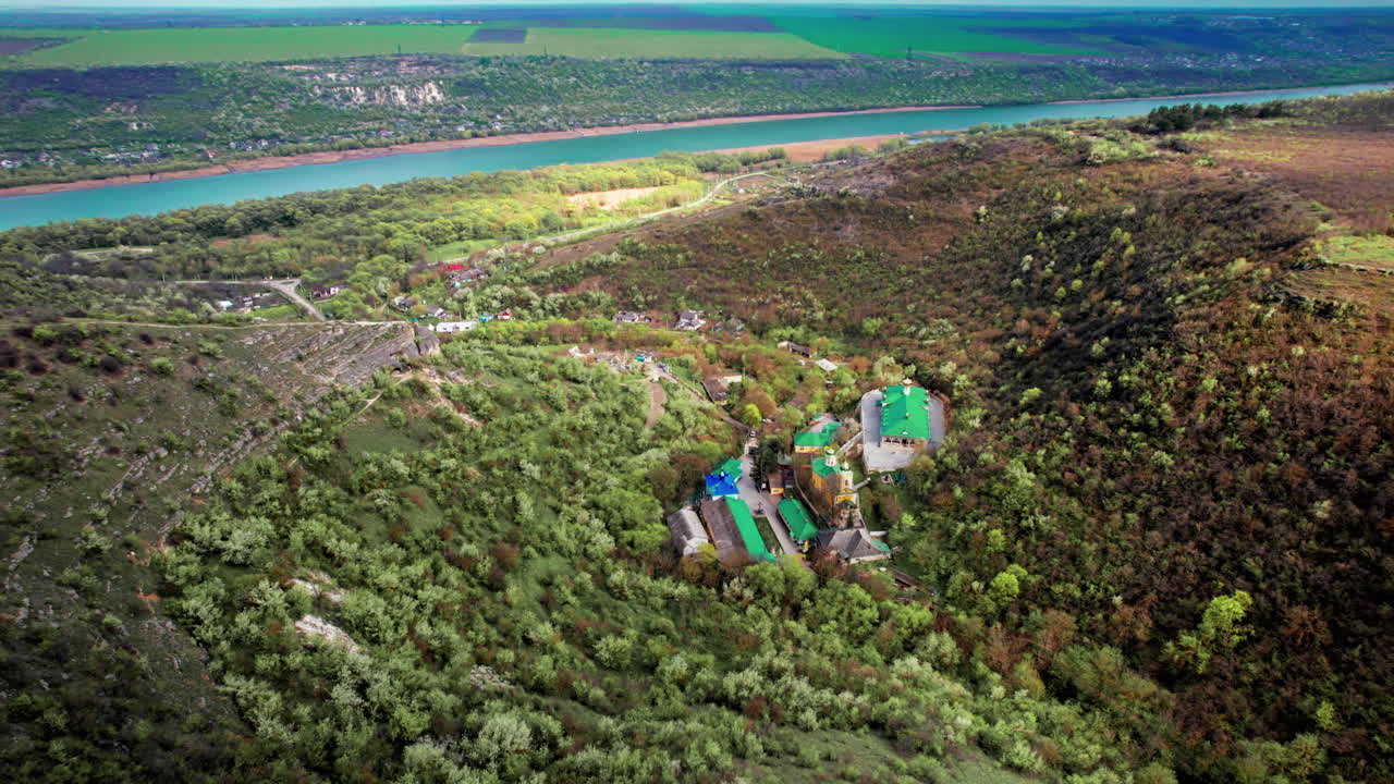 Aerial drone view of Saharna Monastery, Moldova. Monastery with churches located in a valley covered with lush forest. Dniester river on the background