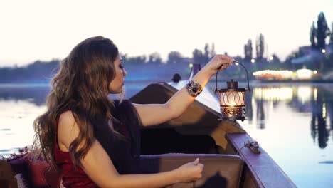 evening view of a woman holding night lamp traveling by boat at sunset. gondola floating along the river with a beautiful female