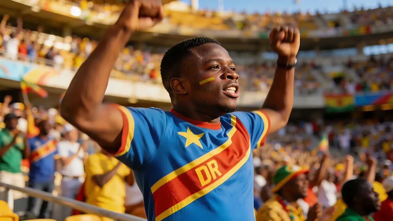 Tifoso maschio che esulta, alzando le braccia e urlando alla ringhiera dello stadio, indossando una maglia della DR e festeggiando un gol.