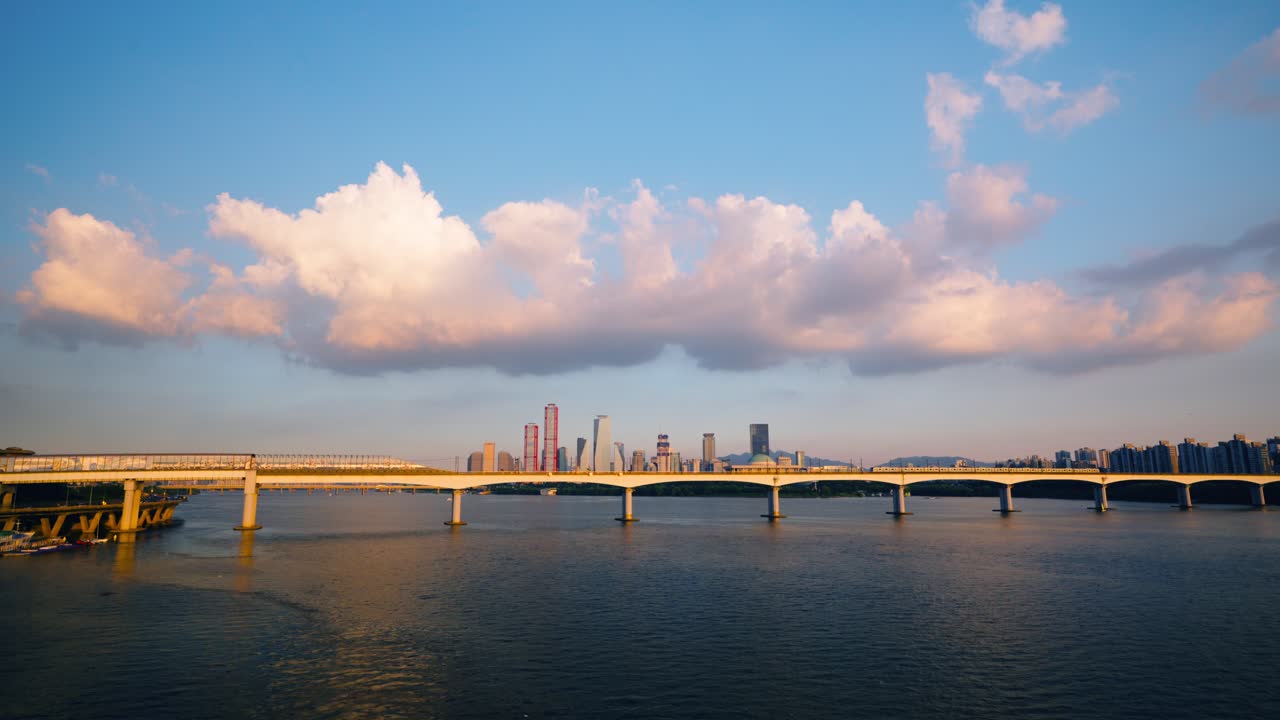Seoul subway line 2 train crossing Dangsan Railway Bridge at sunset, with golden light on the river, purple clouds, and Yeouido financial district skyscrapers in the background - wide aerial
