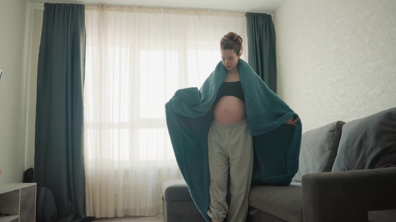 Donna incinta che si avvolge in una coperta e si siede sul divano