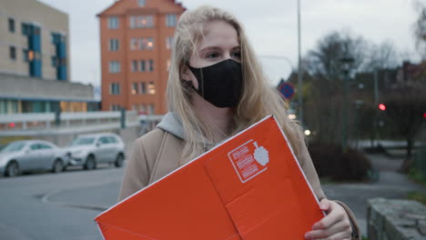 joven rubia con mascarilla negra sosteniendo un paquete