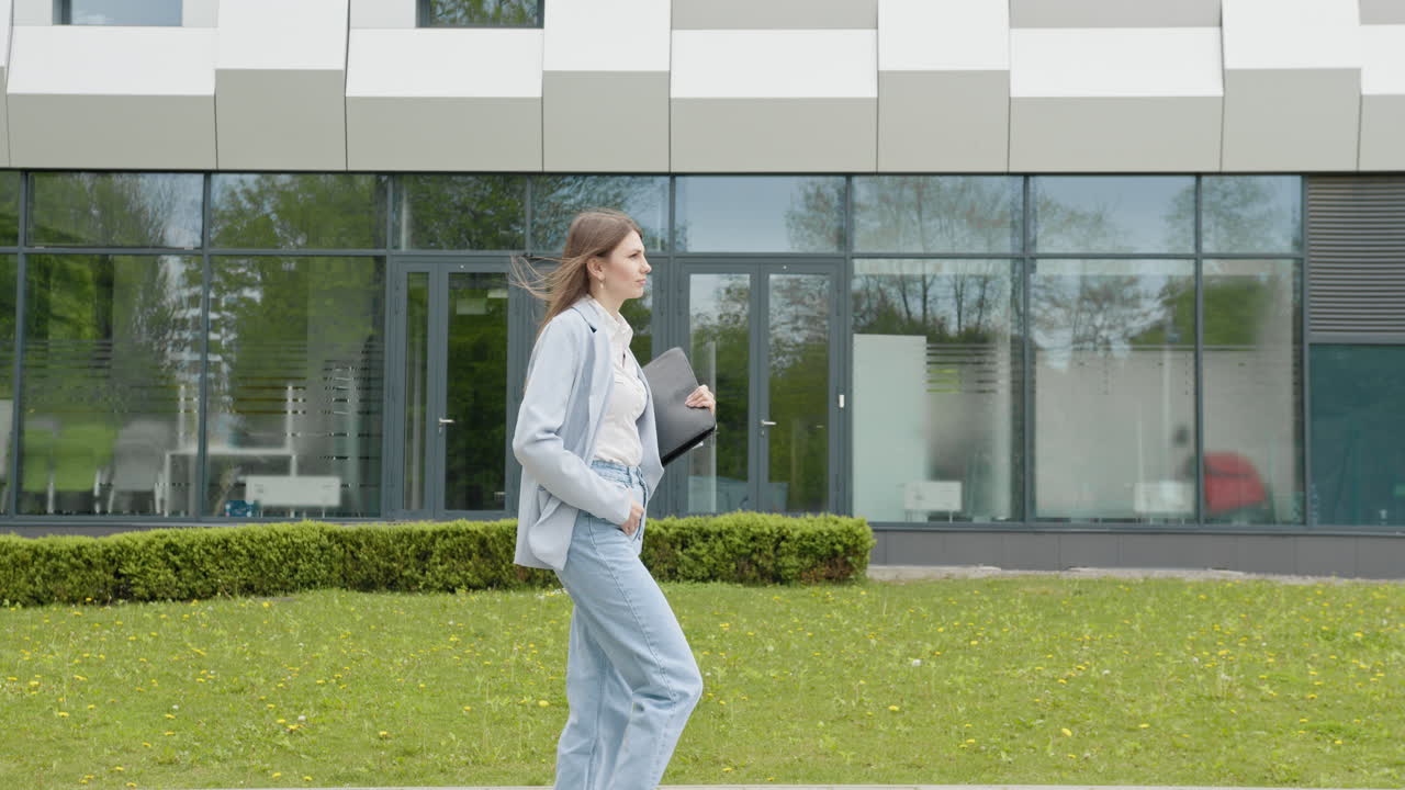 una ragazza in abito da lavoro con un portatile nelle mani cammina per la strada sullo sfondo di un