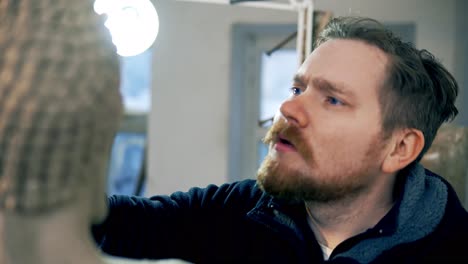 artista concentrado trabajando en la cara de la estatua de buda usando una herramienta especial en el taller