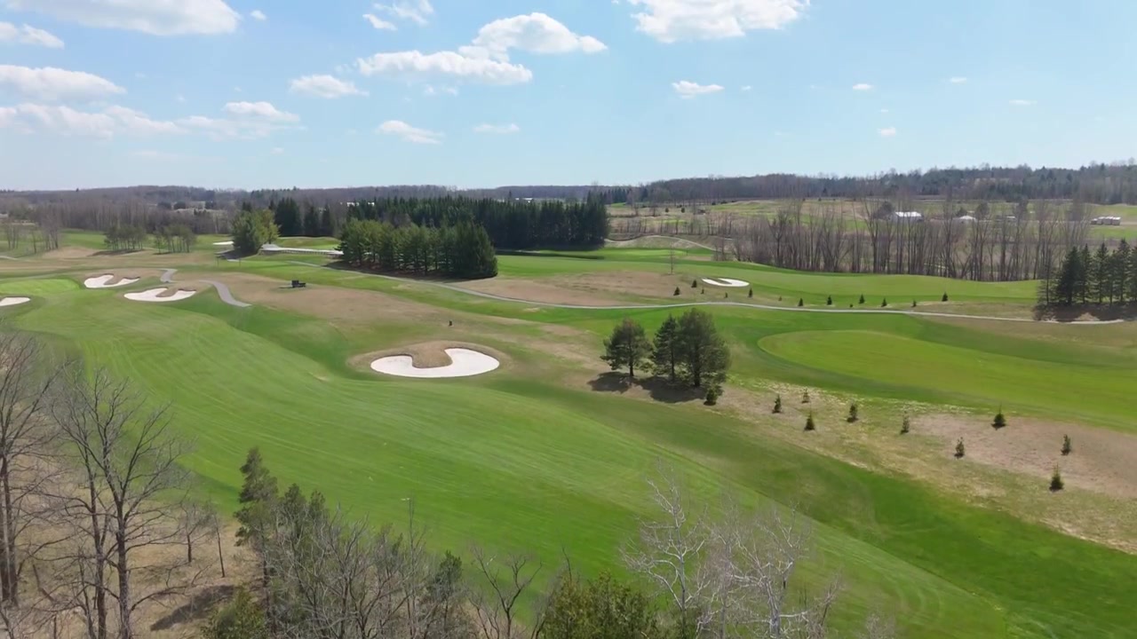 Eine Drohne steigt über TPC Osprey Valley auf und enthüllt Fairways, die von dichten Bäumen gesäumt sind, unter einem strahlenden Himmel. Ideal für Golf-Werbung oder Landschaftsaufnahmen.