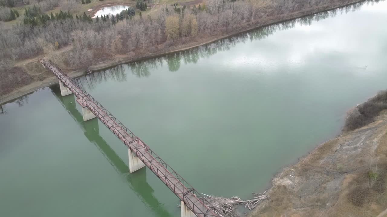 2-3 vista de pájaro volar sobre el puente peatonal en el parque sobre el estanque y un río contaminado en el otoño sin nadie a la vista aceptar una casa de castores al pie del puente un ganso canadiense dormido