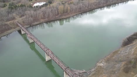 2-3-Blick-Aus-Der-Vogelperspektive-Fliegen-Sie-über-Eine-Fußgänger-Fachwerkbrücke-Im-Park-über-Einen-Teich-Und-Einen-Verschmutzten-Fluss-Im-Herbst,-Ohne-Dass-Jemand-In-Sicht-Ist.-Akzeptieren-Sie-Ein-Biberheim-Am-Fuß-Der-Brücke-Schlafende-Kanadische-Gänse