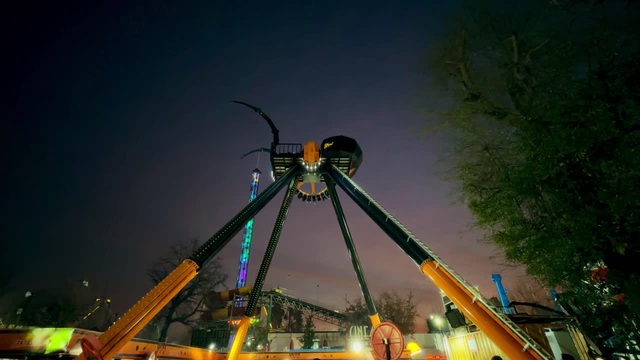 Wide angle view of the Spider ride at night at Fantasilandia amusement park, Santiago, Chile. Giant hammer shaped game with pulley.