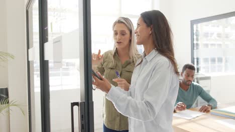 mujeres de negocios ocupadas discutiendo el trabajo con la tableta en la pared de vidrio en cámara lenta