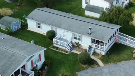 typical mobile home in mobile trailer home park, american flag, blue siding and gray shutters, white deck and porch railing handicapped accessible disability ramp entrance in usa, united states aerial