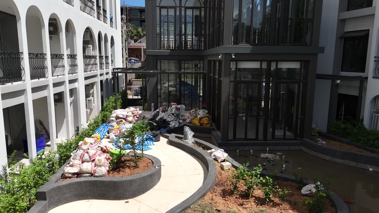 An outdoor courtyard area with construction materials and an unmaintained pond between modern buildings