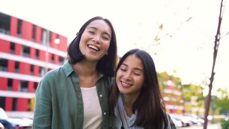 two happy japanese female friends laughing and making v sign while looking at camera in the street