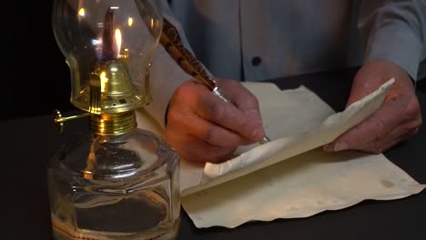 persona escribiendo con pluma junto a una lámpara de aceite