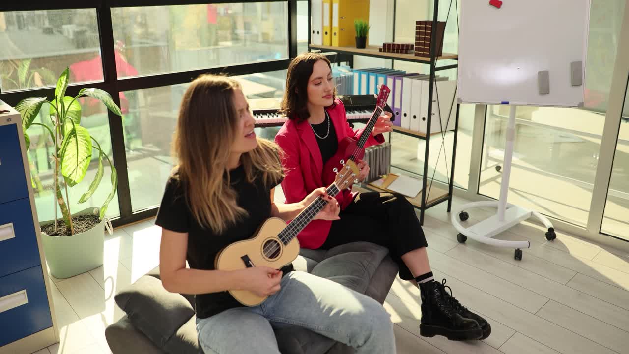 Duas Jovens Mulheres Tocando Ukuleles e Cantando em um Escritório Moderno