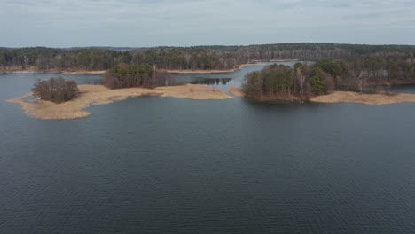 AERIAL:-Isolated-Little-Islands-in-the-Lake-with-Reeds-Waving-in-the-Wind-and-Forest-in-the-Background