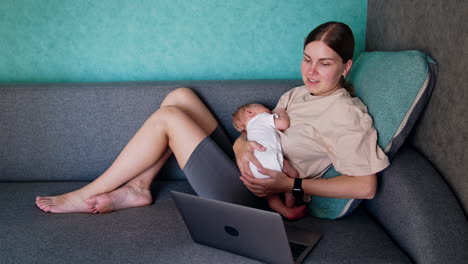 caucasian mother combining work and childcare. woman with child in arms works at laptop.