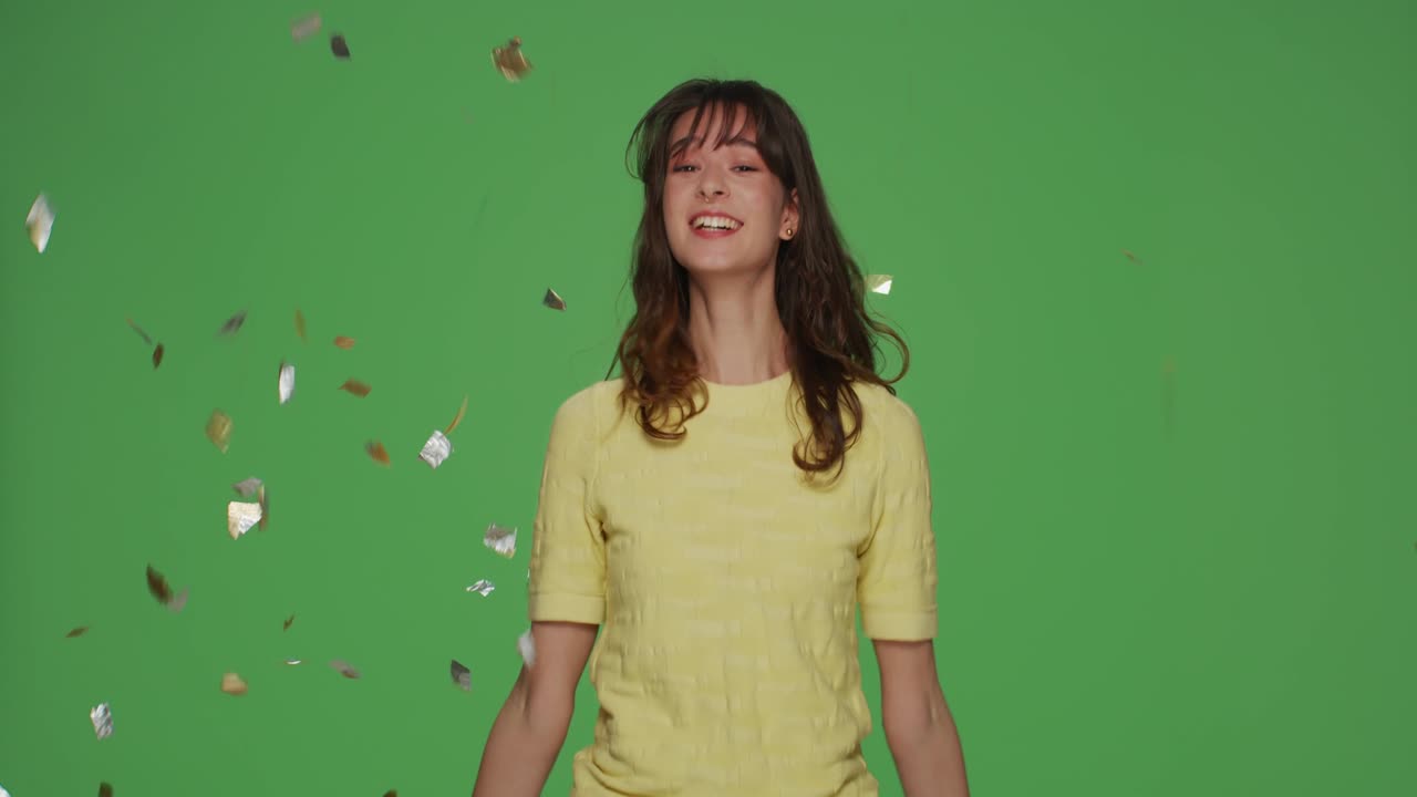 joven feliz saltando bajo confeti brillantes lluvia, celebrar las vacaciones, divertirse en chroma clave de fondo verde