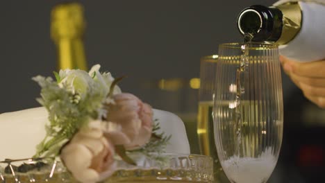 Close-Up-Of-Person-Pouring-Champagne-Into-Glass-At-Table-Set-For-Meal-At-Wedding-Reception-4