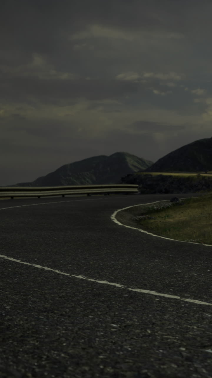 Curving road along mountains under cloudy sky in late afternoon light