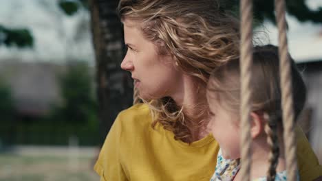 close up of mom with little girl swinging and talking together in summer day.