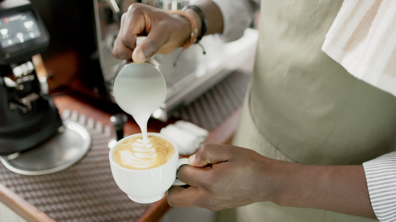 African American barista pours milk into a coffee cup, creating latte art