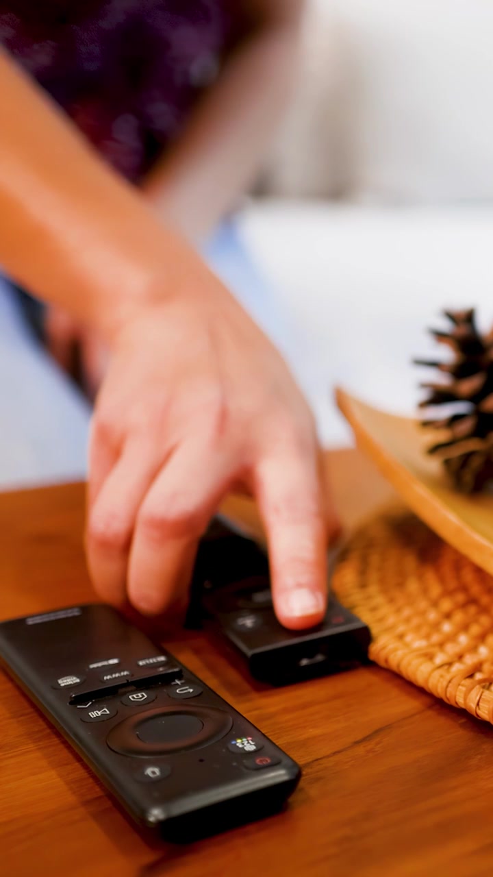Una mano si allunga e prende un telecomando nero da un tavolo di legno.