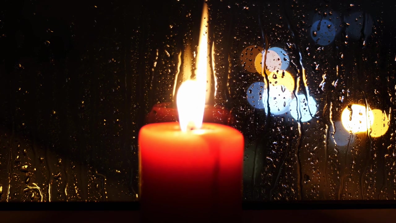 Fiamma tremolante di candela contro una finestra piovosa con bokeh della città