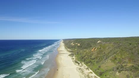 Breathtaking-aerial-view-along-the-broad-golden-sands-of-Fraser-Island,-as-a-single-four-wheel-drive-car-makes-its-solitary-way-up-the-beach