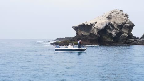 aerial orbit of a boat anchored in the waters near the rocky coast of coronado islands, mexico as friends cast and fish off the front