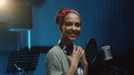 close up of the pretty young female singer in stylish look smiling cheerfully to the camera at the microphone at therecording sound studio