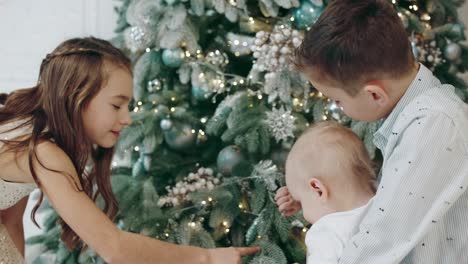 Three-cute-kids-walking-around-christmas-tree-in-living-room.