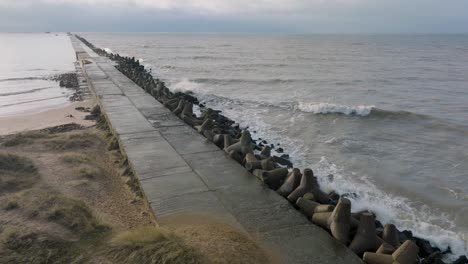 aerial establishing view of port of liepaja concrete pier, baltic sea coastline day, big waves splashing, slow motion drone shot moving forward