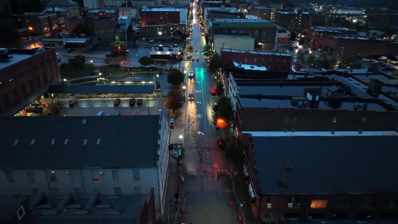 Aerial birds eye shot over main street of american town at night. Rainy day in historic city with lighting shopping street. Parking cars in area. Housing area and apartments. Wide shot.