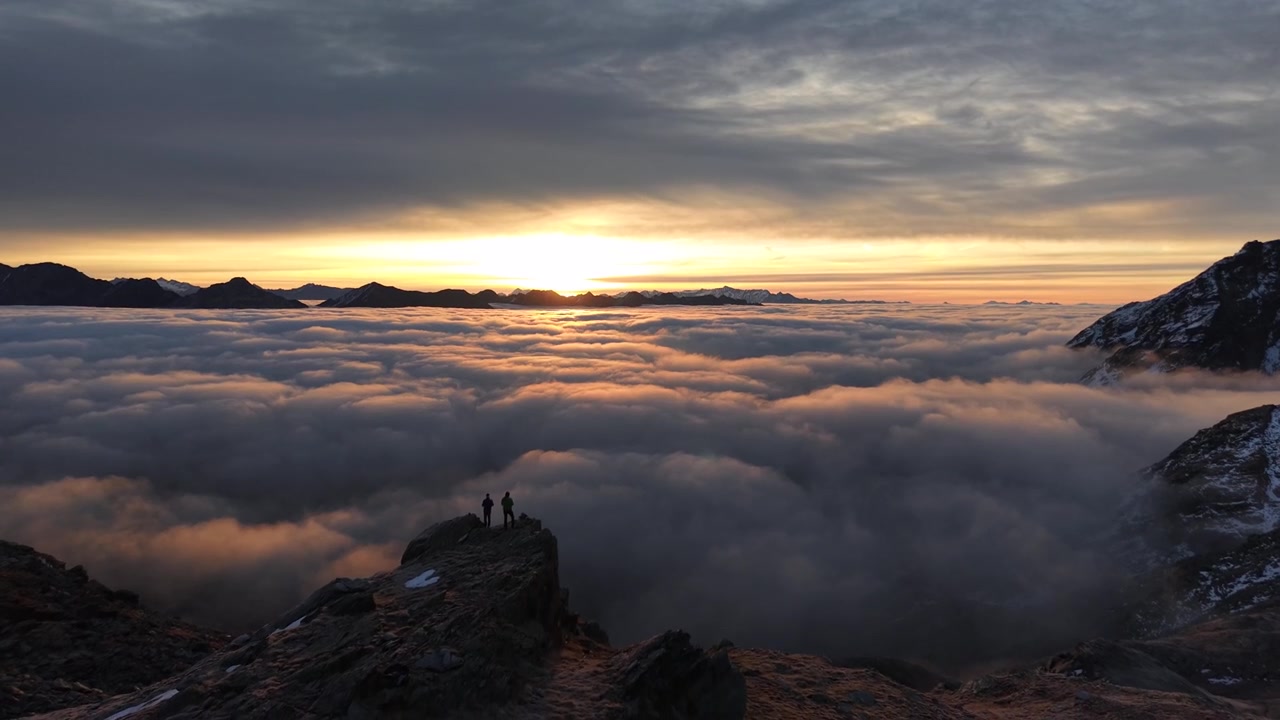 Sorvolo aereo su escursionisti che si godono il bagliore dell'alba sopra l'inversione delle nuvole nelle Alpi svizzere con una vista panoramica in picchiata delle montagne e del cielo colorato