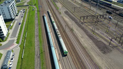 disparo aéreo escénico de un tren de pasajeros que conduce hacia el atardecer en vías de tren rodeadas de árboles por encima del paisaje urbano hacia adelante