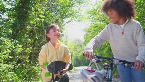 Junge-Mit-Fahrrad-Und-Mädchen-Mit-Skateboard-Gehen-Gemeinsam-Die-Landstraße-Entlang