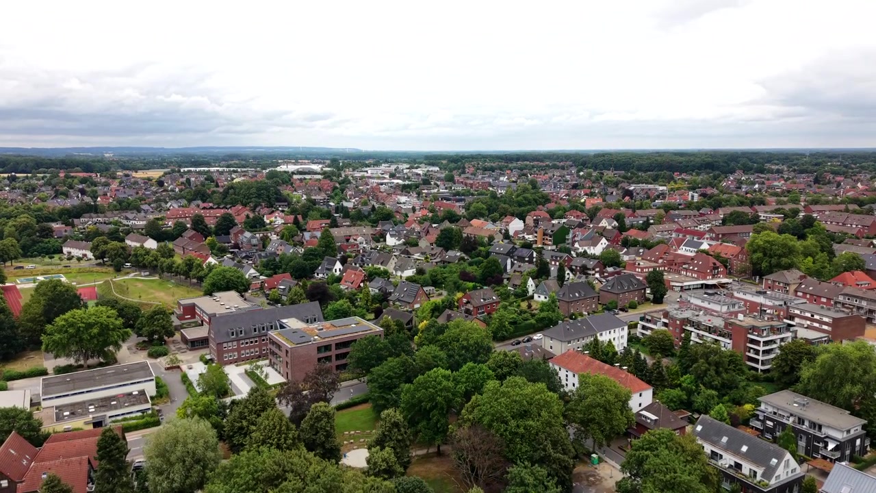 Dichte deutsche Stadt breitet Ziegeldächer unter bedecktem Sommerhimmel aus, historische Giebelhäuser gruppieren sich unter dichtem Blätterdach entlang gewundener Wohnstraßen. Luftaufnahme mit Drohne, weite Einstellung