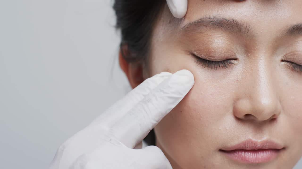 회색 배경에 있는 아시아 여성의 얼굴을 만지는 장갑을 입은 손, 슬로우 모션