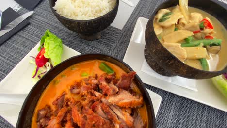 Traditional-Thai-red-curry-crispy-duck-dish-and-green-curry-chicken-with-rice-in-a-coconut-bowl,-Thai-cuisine-restaurant,-4K-top-shot