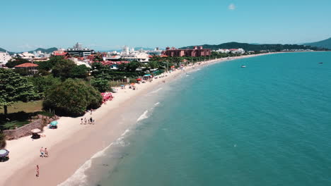 Lateral-drone-view-capturing-the-entire-shoreline-of-Jurerê-Internacional-Beach,-Florianópolis,-showcasing-its-coastal-grandeur